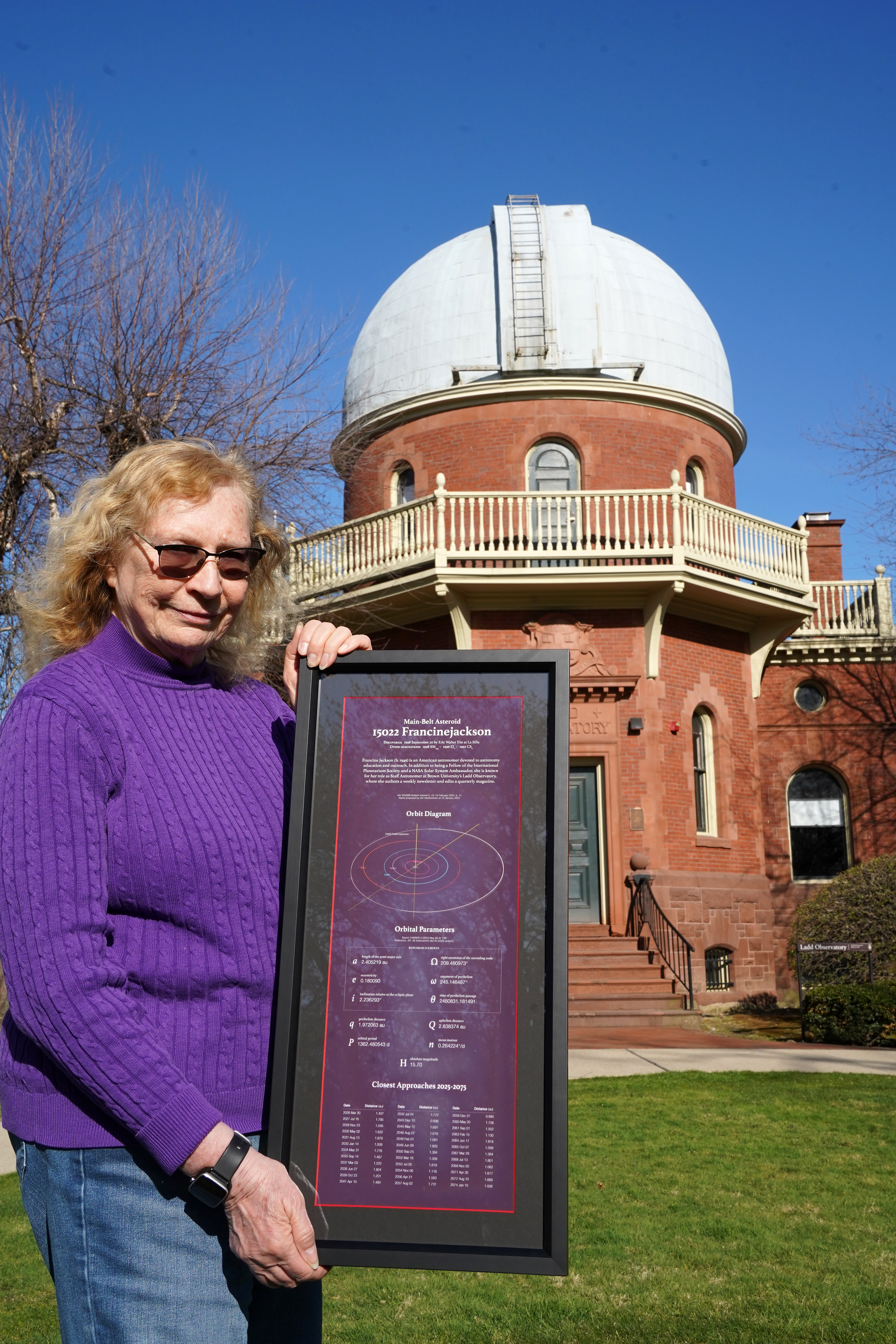 Francine Jackson stands in front of Ladd Observatory with a commemorative display made by Jim Hendrickson that includes technical information, orbit diagram, orbital elements, and closest approaches of asteroid 15022 Francinejackson. 